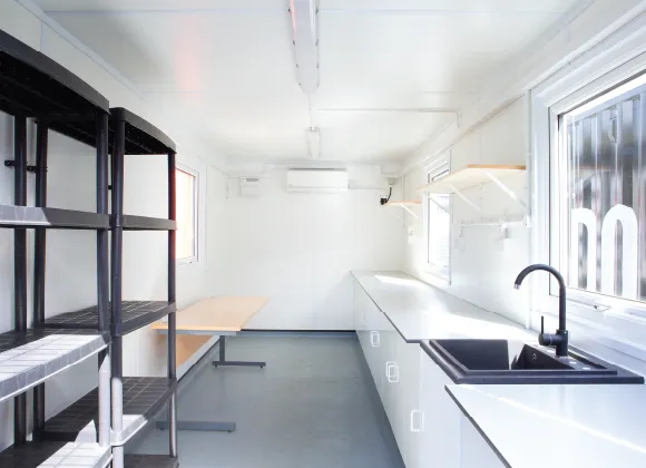 Interior view of a custom container laboratory, featuring fitted worktops, integrated sink, shelving units, windows for natural light, and wall-mounted air conditioning — designed for mobile scientific research by UNDO.