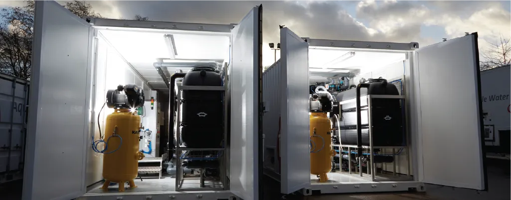 Two open container conversions units for company Veolia revealing industrial equipment inside. The interiors are illuminated, showing tanks, pipes, and filtration systems. The scene is set outdoors, with a cloudy sky in the background.