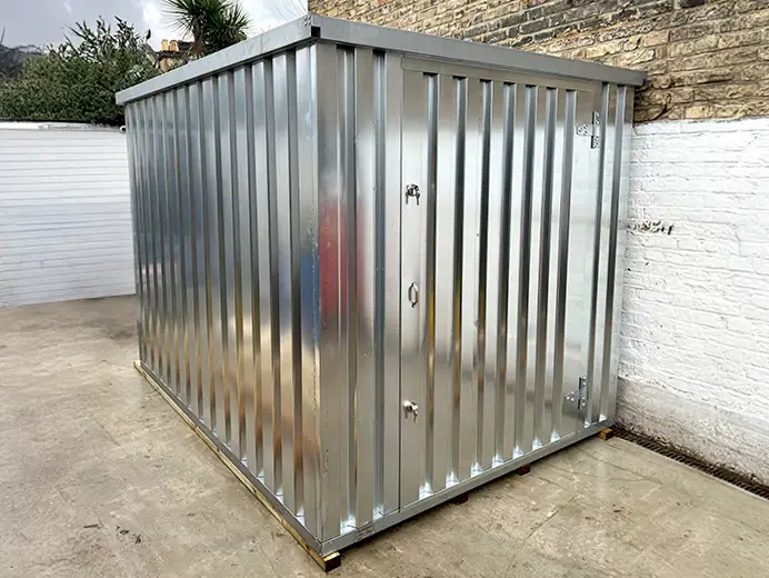 A galvanised flat pack metal storage shed installed in a small outdoor space against a brick wall, with corrugated steel panels and a secure door.