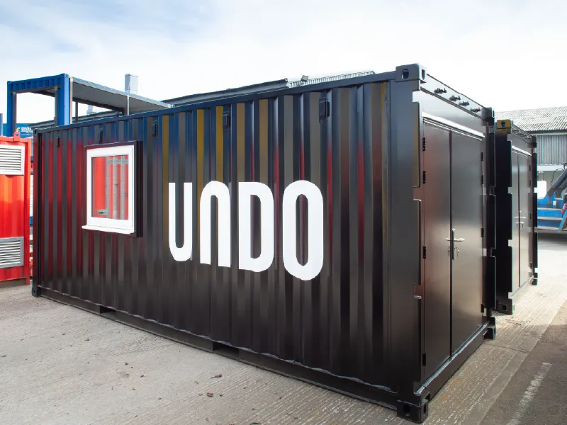 Side view of a black converted container unit with white-framed windows and the full-height "UNDO" branding prominently displayed.