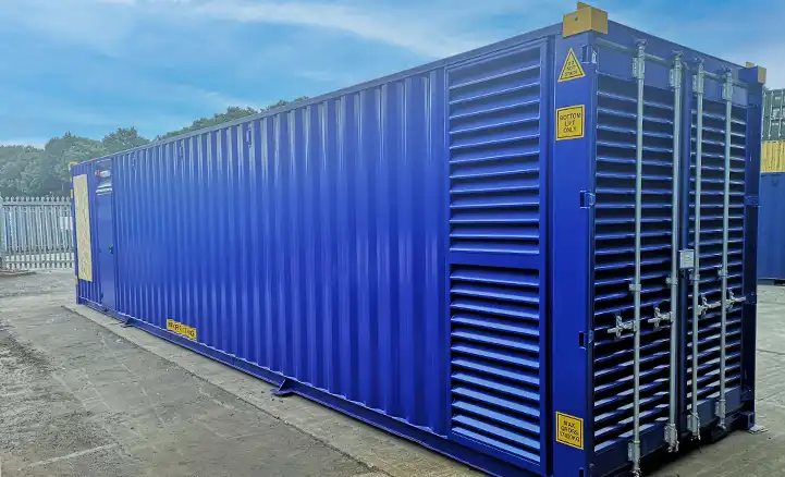 Exterior view of a blue converted shipping container by S Jones Containers, customised to house switchgear equipment. The container features large louvered ventilation panels, secure double doors, and warning signage, situated in an industrial yard.