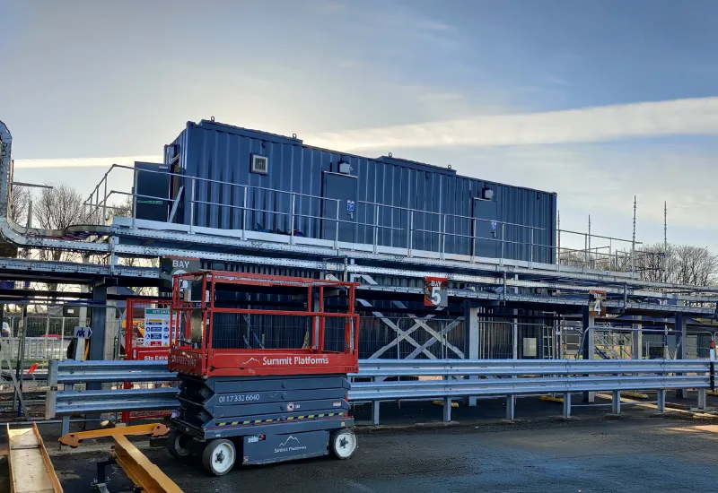 Large-scale generator housing built from converted shipping containers, elevated on steel platforms with access walkways for industrial energy infrastructure.