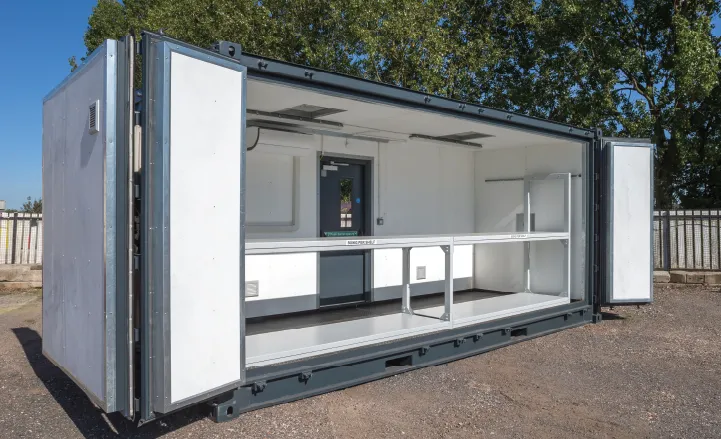 Interior view of a dark grey battery storage container conversion with one long side fully open. The inside is clean and white with built-in shelving, lighting, and access to a rear door.