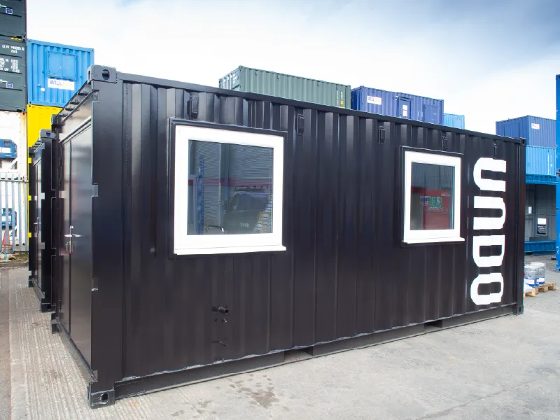 External view of a sleek black converted shipping container with two white-framed windows and the bold white "UNDO" branding painted on the side.